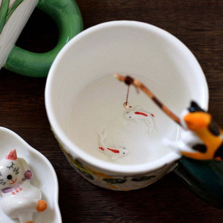 Cat Go Fishing handmade ceramic coffee mug, Calico Cat sitting on the mug with fishing rod in it's hand, 2 fish swimming at the botton of the mug