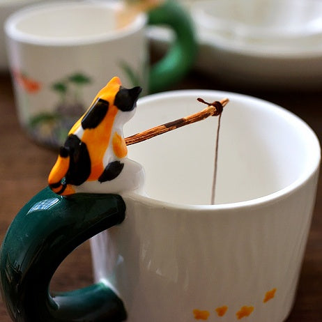 Cat Go Fishing handmade ceramic coffee mug, White Mug, Calico Cat sitting on the mug with fishing rod in it's hand.