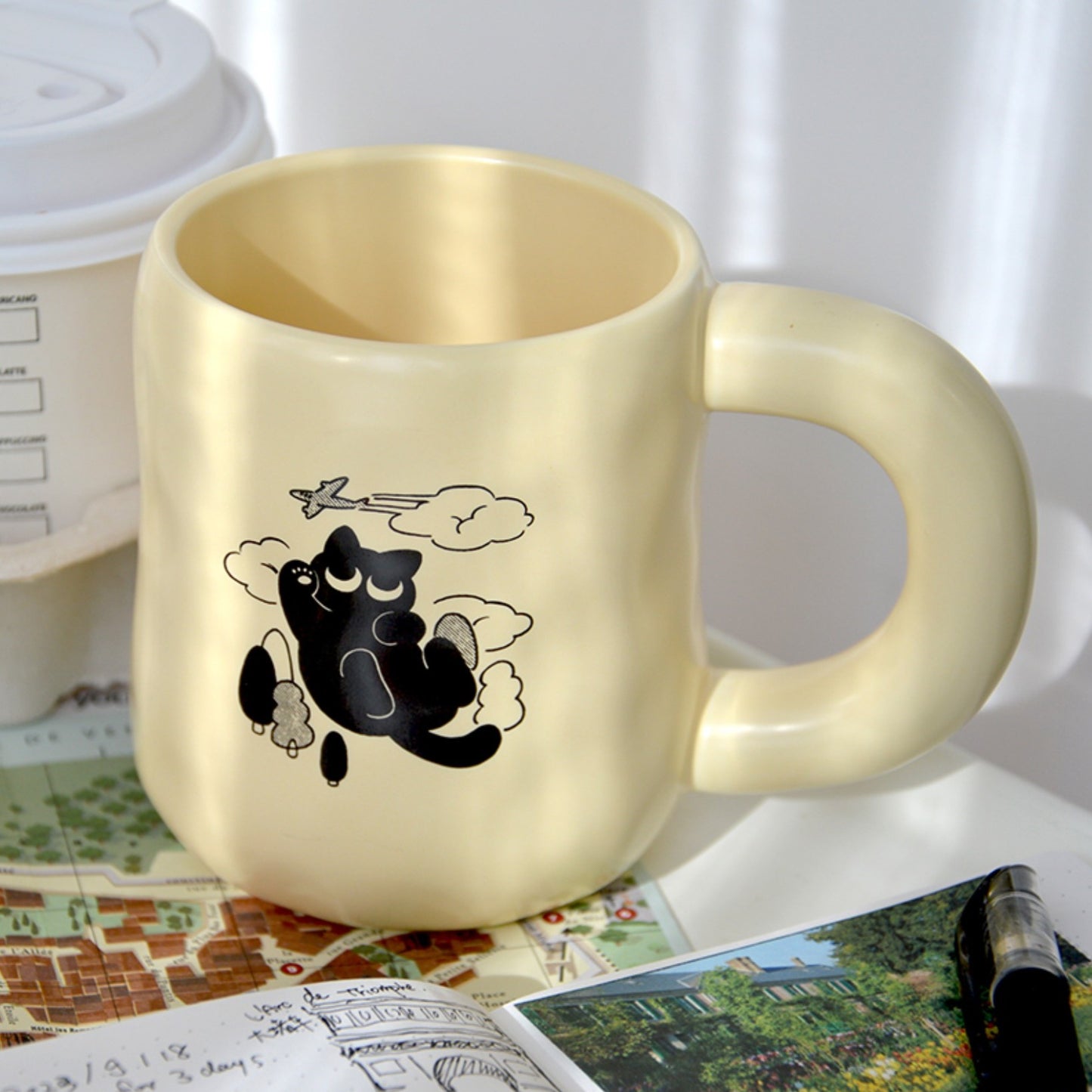 Black Cat's Travel Coffee Mug, cream color with lid, cute black cat illustration with trees and airplane. purrfect gift choice for cat lovers