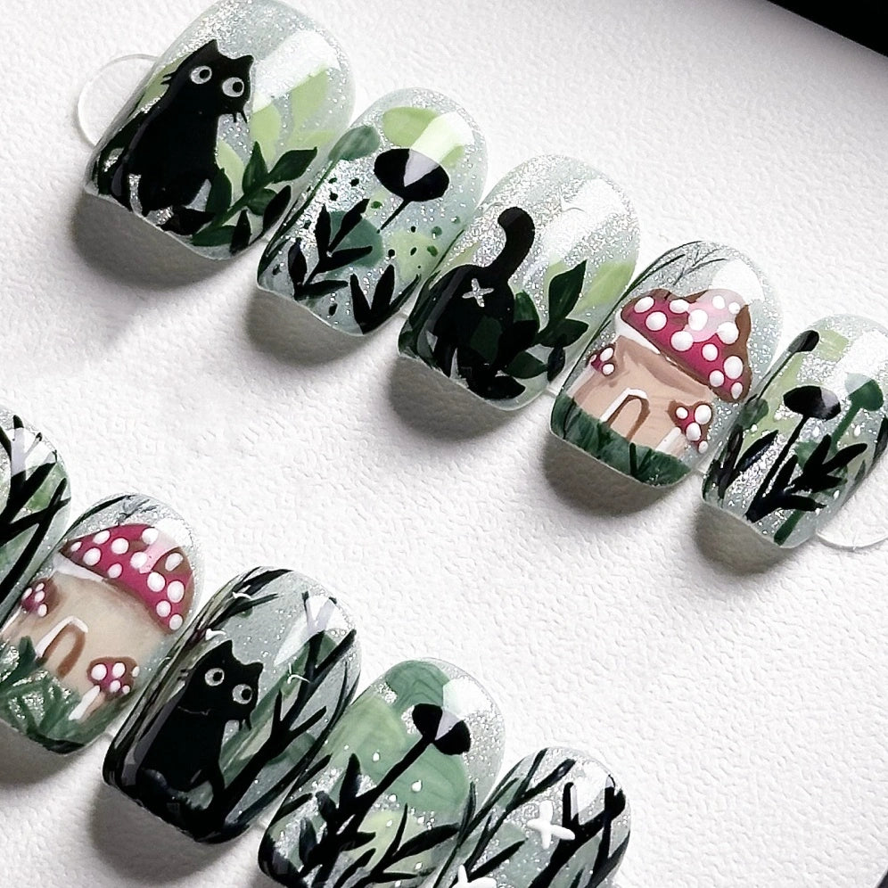 Handmade press-on nails with a black cat in a magical forest, surrounded by mushrooms and greenery, from the Whiskers in Wonderland collection.
