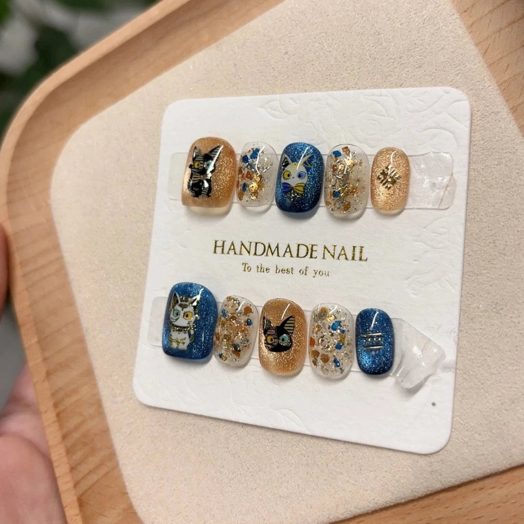 Egyptian cat-eye press-on nails featuring the Paws of the Pharaoh design, with playful cats and sparkling gold accents for a unique nail art look.
