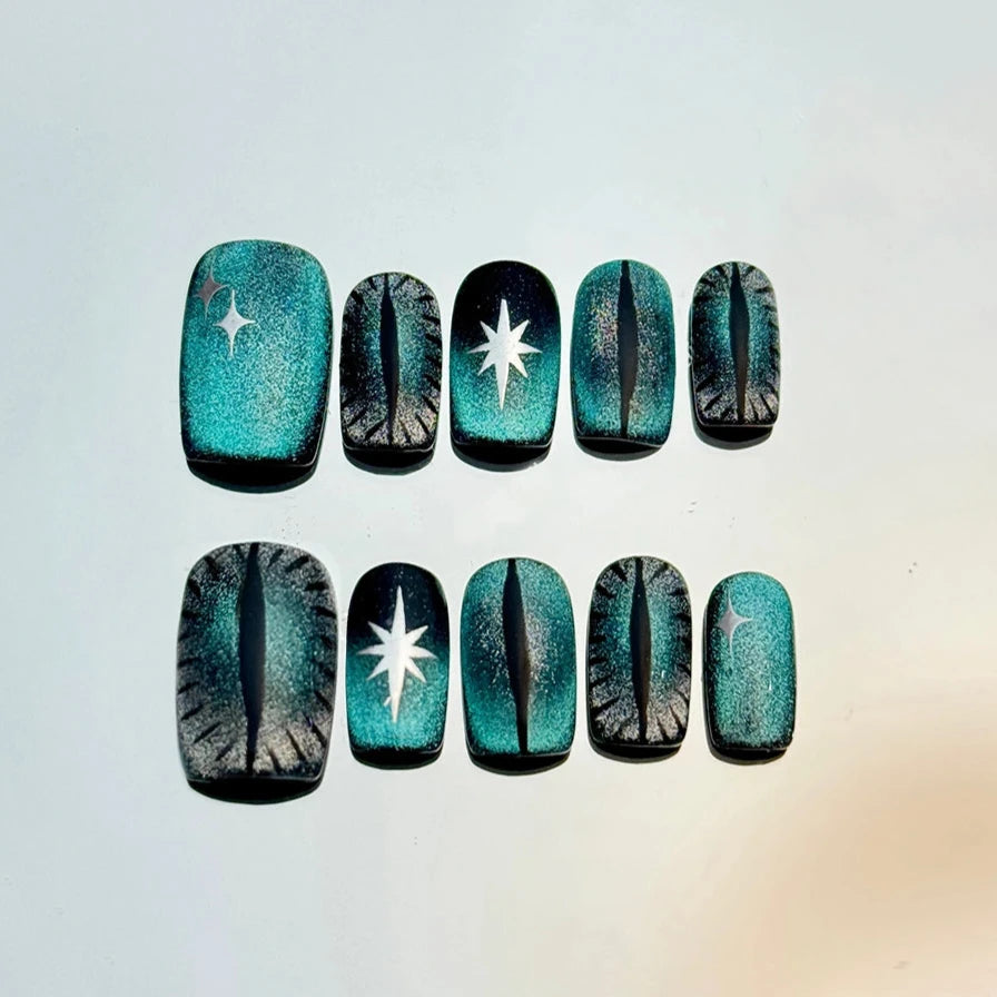 Mystic Cat-Eye Glam handmade press-on nails with a teal and black glittery base, featuring black cat-eye designs and silver embellishments. Perfect for Halloween cat lovers.
