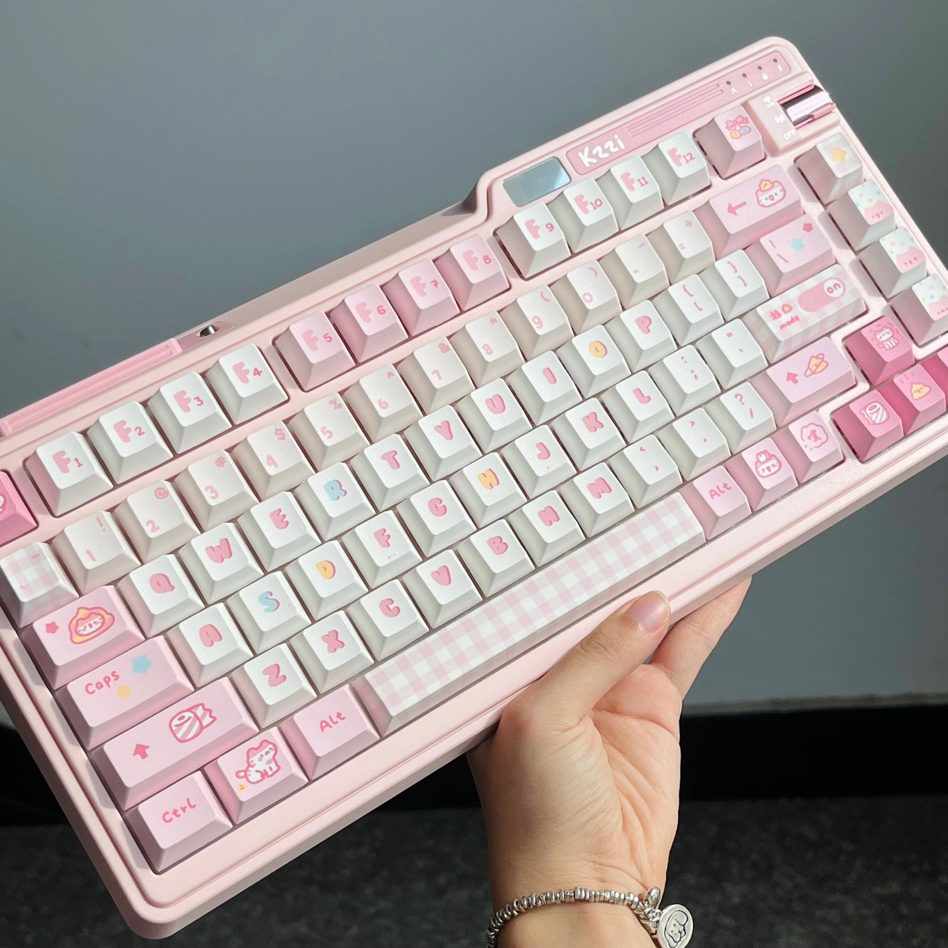 Handheld view of the Pooping Kitty Keycap Set showcasing the pink and white color scheme with toilet-themed cat designs.